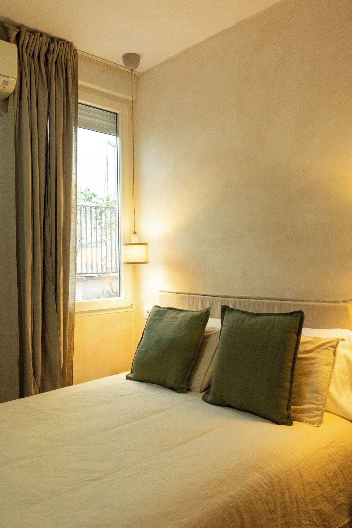 Una camera d'albergo con un letto, tende, una finestra e una lampada a parete.