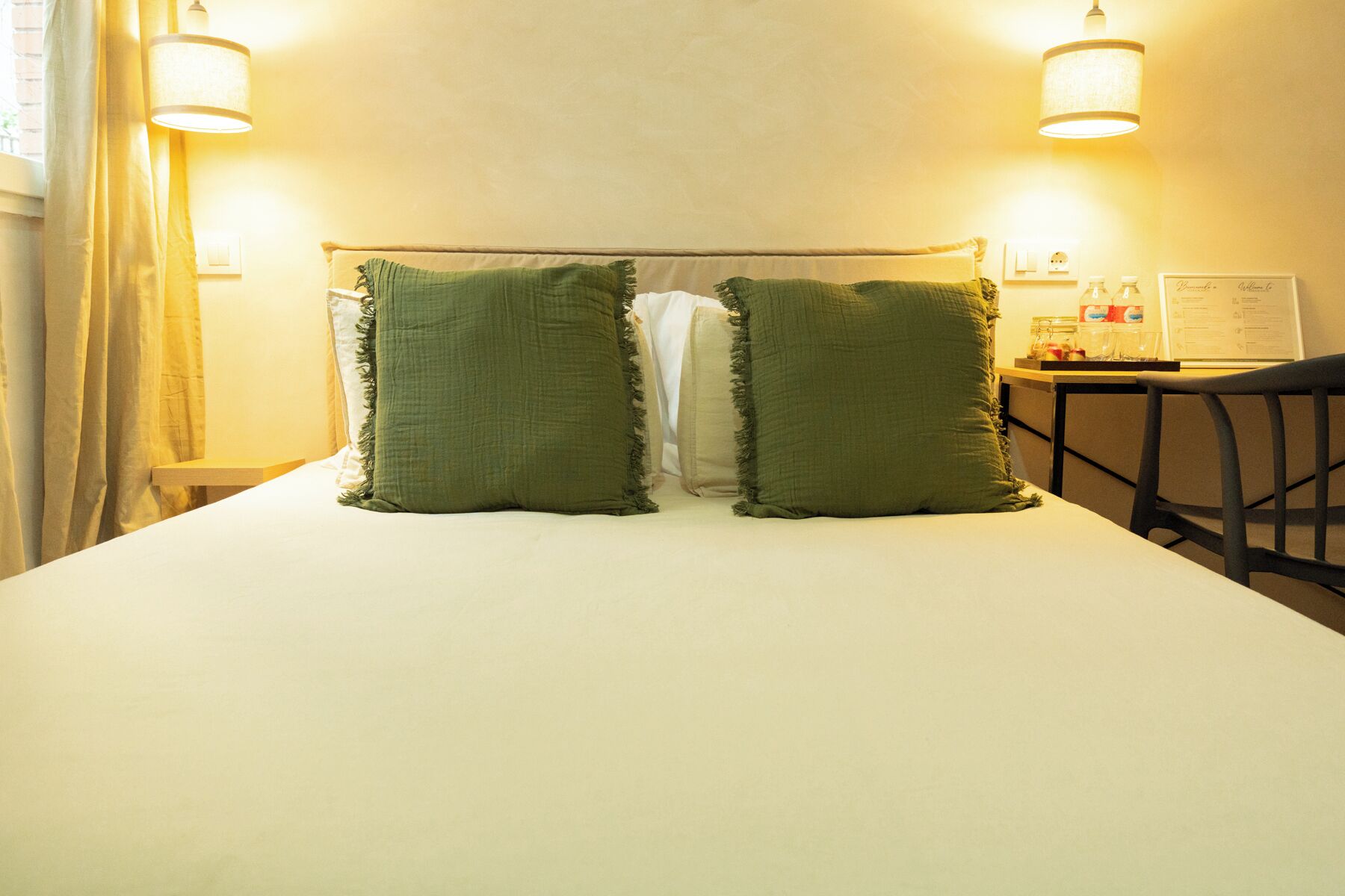 A bed with two green pillows, a nightstand with a lamp, and a chair.
