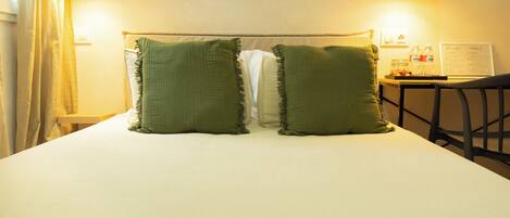 A bed with two green pillows, a nightstand with a lamp, and a chair.