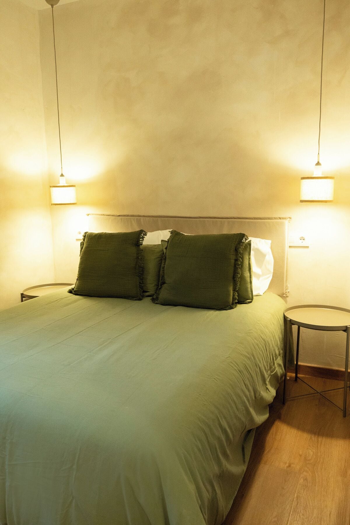 Una cama con cabecera, dos mesitas de noche y dos lámparas fijadas a la pared.