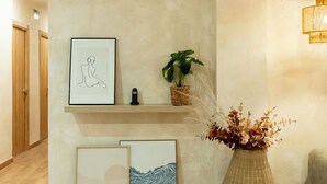 Un espace d’accueil doté d’un plancher en bois, d’une étagère murale ornée d’œuvres d’art encadrées, d’une plante en pot et d’une chaise en osier.