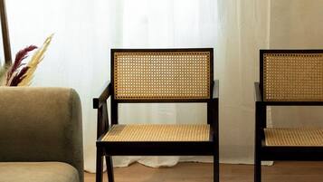 Ein Zimmer mit zwei dunklen Holzstühlen, die gewebte Sitzflächen und Rückenlehnen haben, einem beigefarbenen Sofa und einem hellen Teppich.