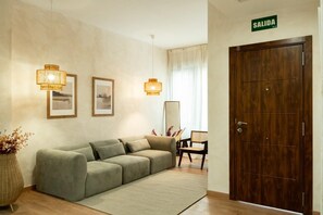 Eine Hotelhalle mit einer Couch, zwei Wandlampen, einem Spiegel, einer Holztür mit der Aufschrift "SALIDA" und einer Vase mit getrockneten Blumen.