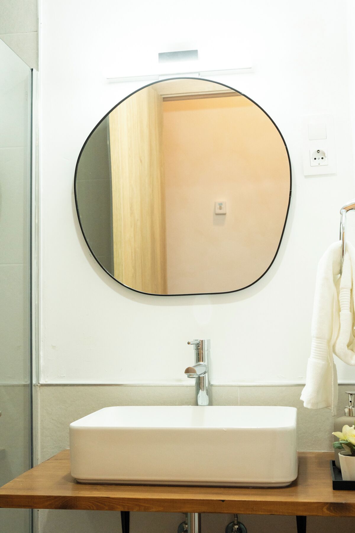 Un bany amb un mirall rodó, un lavabo rectangular i un suport per a tovalloles.