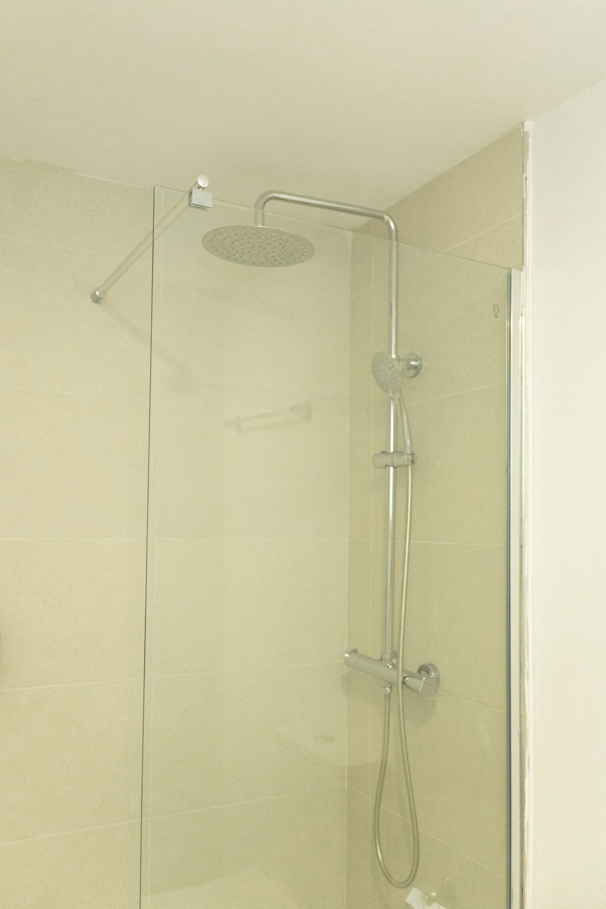 Cabina de ducha con paredes de vidrio, cabezal de ducha de mano y ducha de lluvia superior.