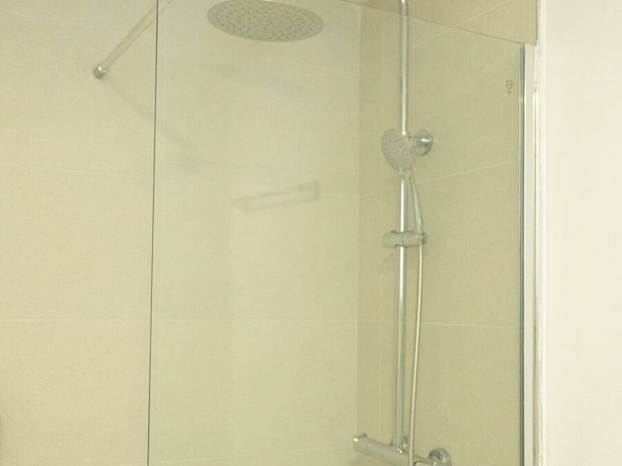Cabina de ducha con paredes de vidrio, cabezal de ducha de mano y ducha de lluvia superior.