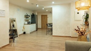 Un vaste espace de vie doté d’un plancher en bois, une cuisine équipée d’un réfrigérateur, un coin repas avec des chaises et un grand miroir.
