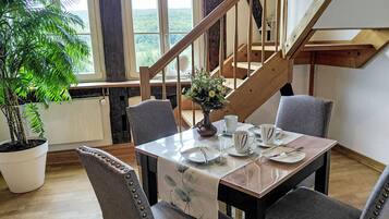A dining area with a table set for four, surrounded by chairs with decorative studs. A potted plant is visible to the left, and a staircase leads to an upper level.