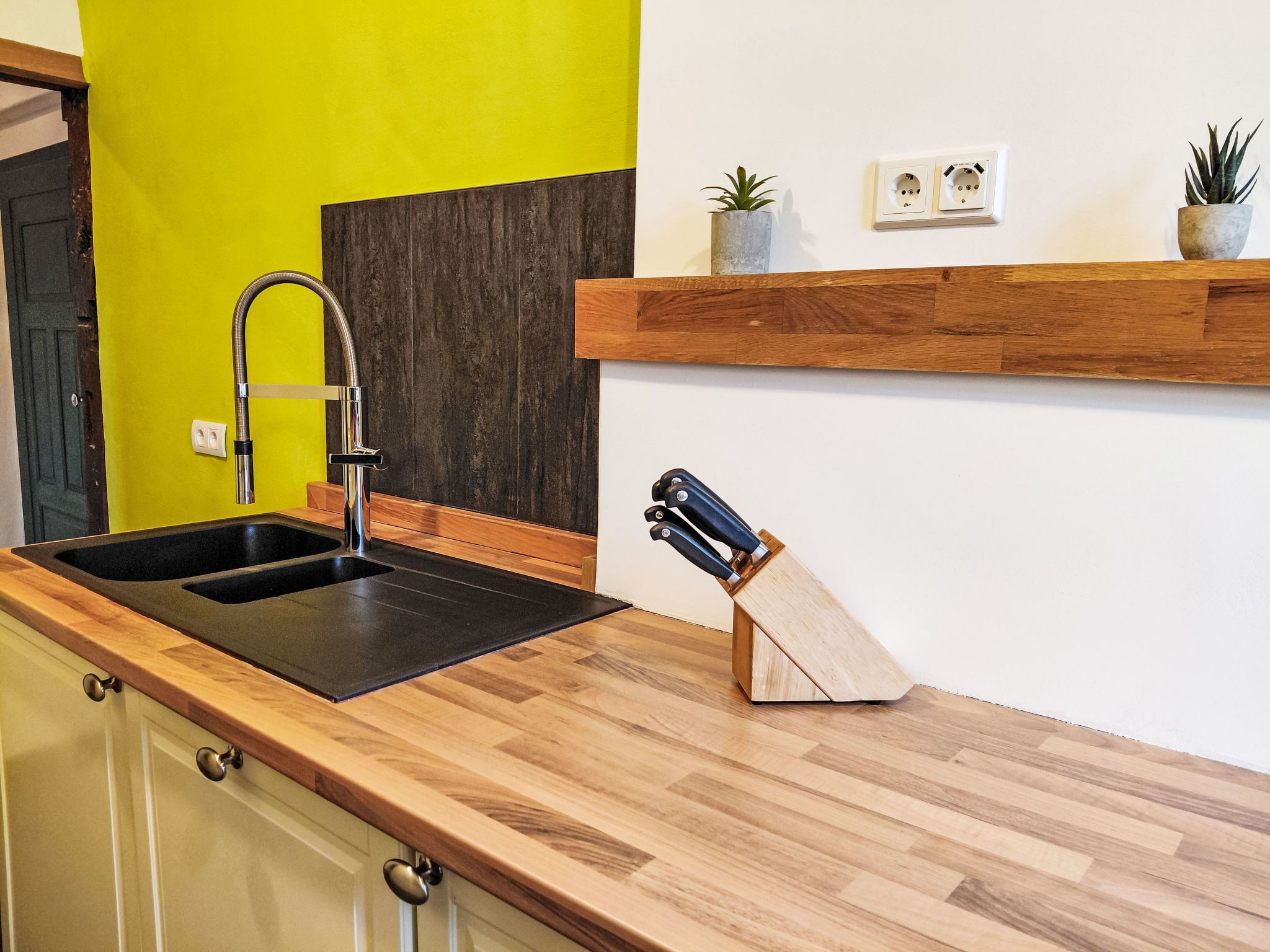 A kitchen with a black sink, wooden countertop, and a knife block.