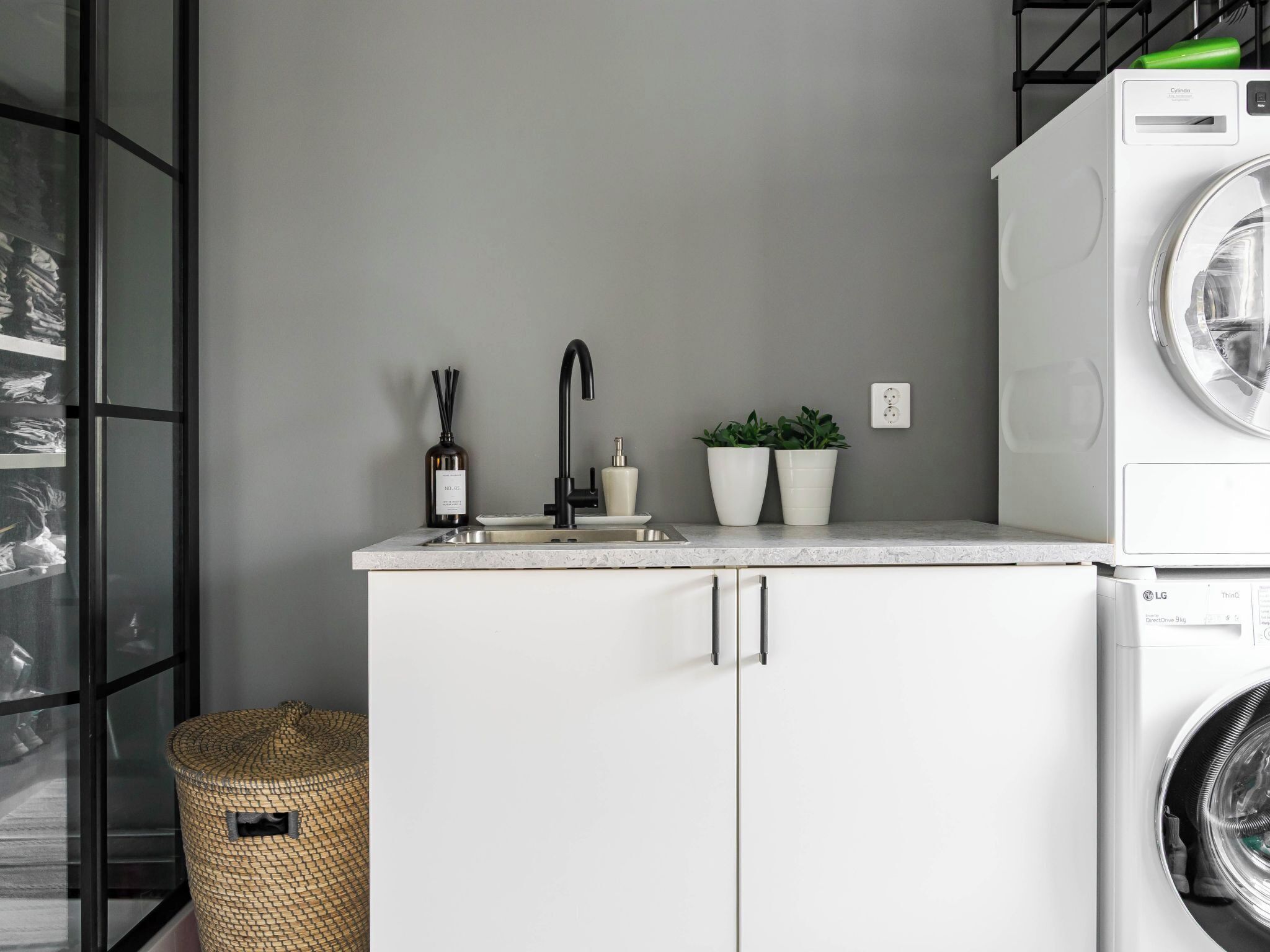 Cocina compacta con lavadora, lavamanos y dos plantas en macetas.