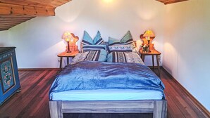 A bedroom with a sloped ceiling, a bed with a blue bedspread, two bedside tables with lamps, and a decorative wall piece.