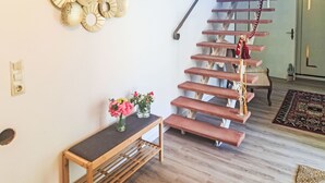 A staircase with wooden steps and a metal handrail, leading to a door. A small bench with a vase of flowers is placed in the foreground.