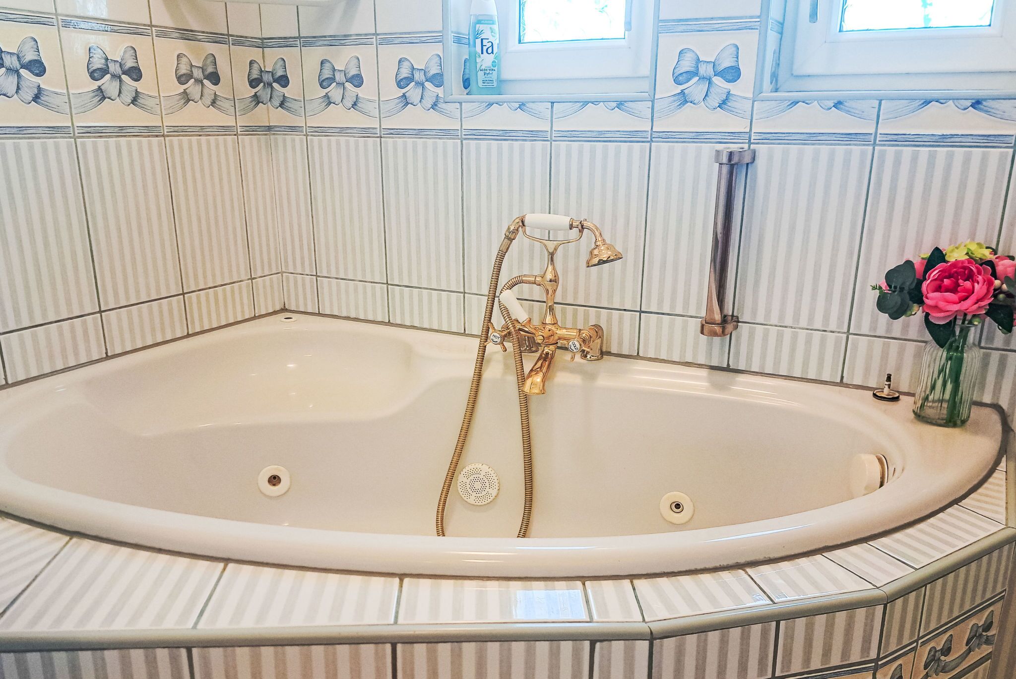 A bathroom with a freestanding bathtub, a handheld showerhead, and a bottle of shampoo on the wall.