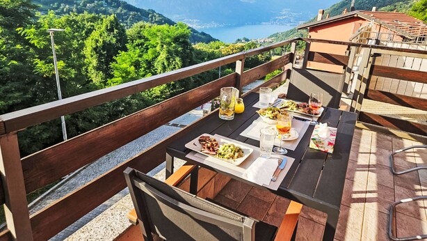 Una terraza con mesa lista para comer, con vistas a un paisaje montañoso y un lago.