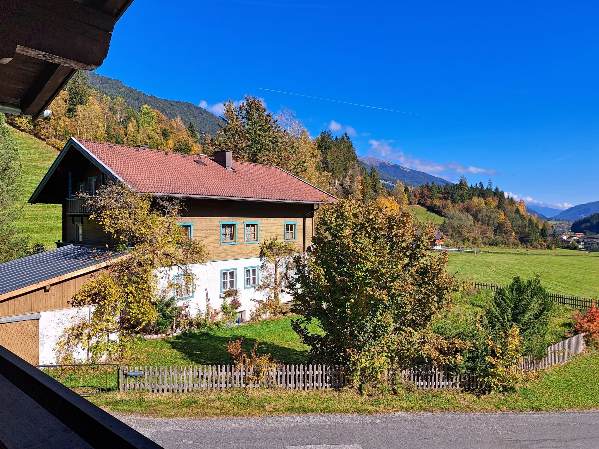 Ein zweistöckiges Haus mit geneigtem Dach, umgeben von einem eingezäunten Garten und mit Blick auf eine Berglandschaft.