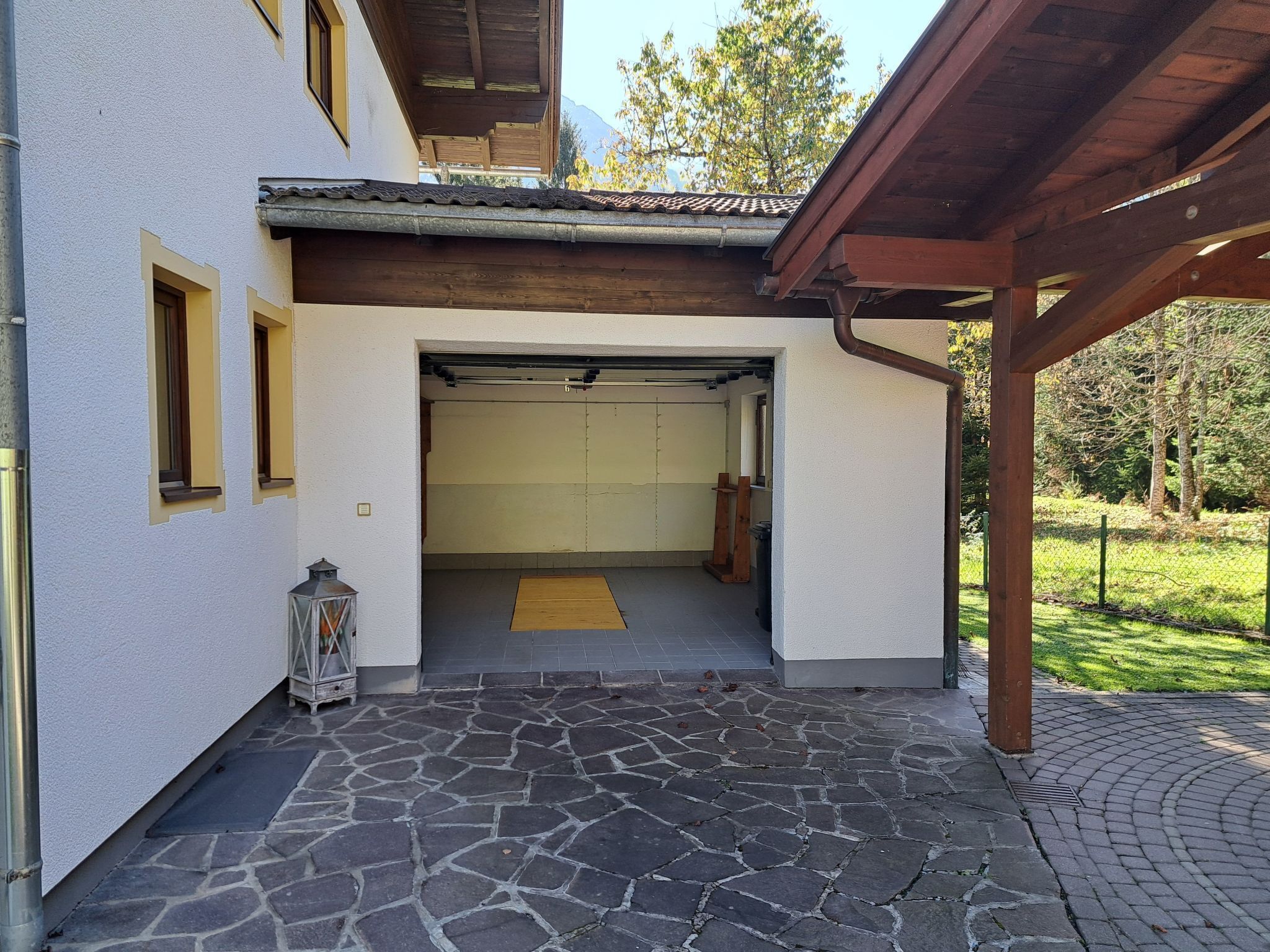Entrada de garaje cubierta con un camino de entrada empedrado que conduce a un edificio blanco con vigas de madera y techo de tejas.