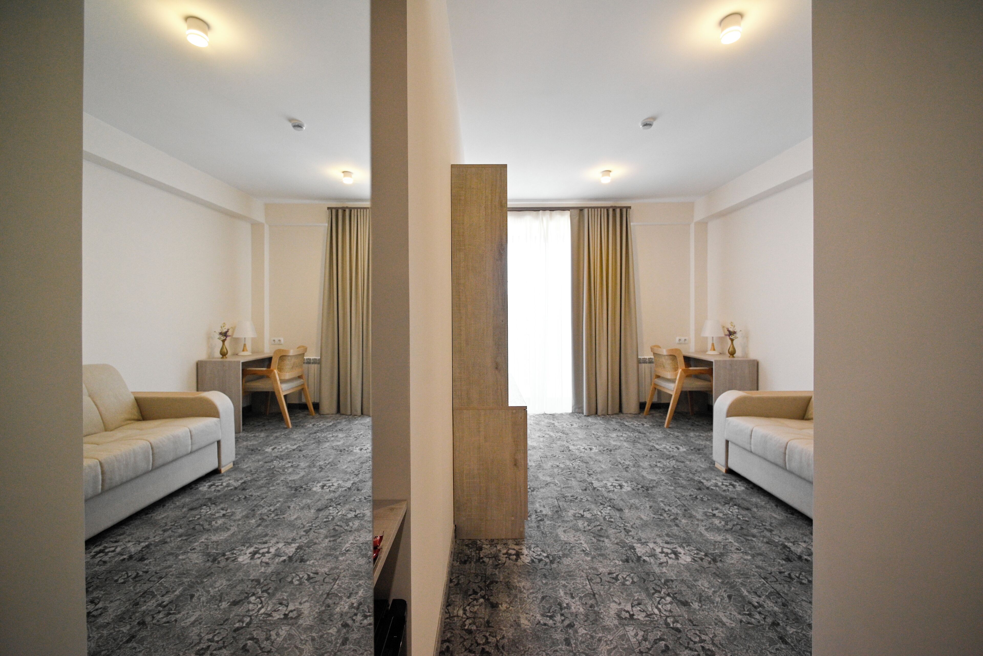 A hotel room with two sofas, a desk, and a large window with curtains.