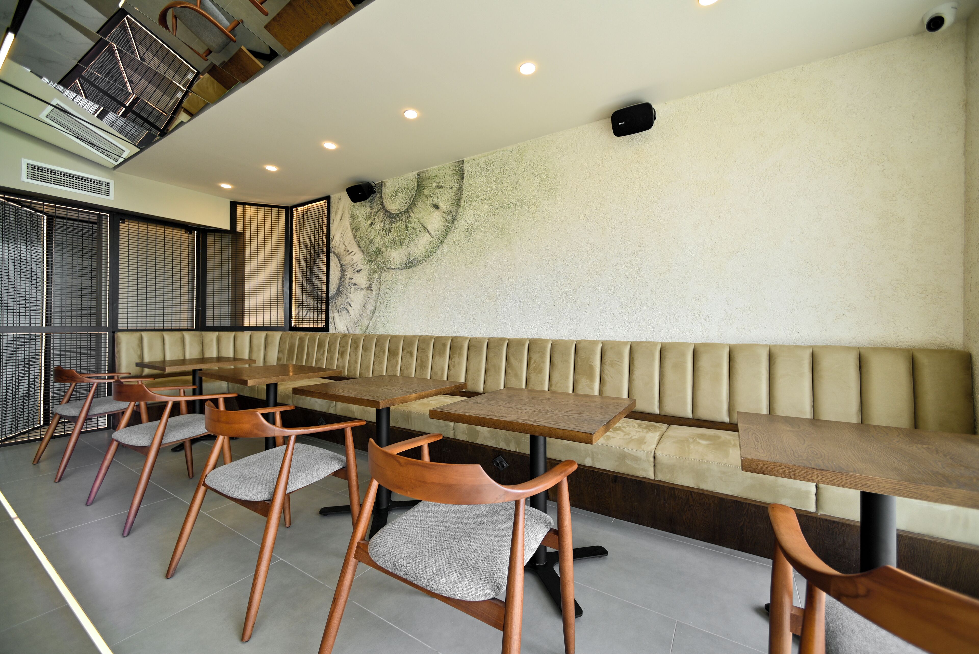 Un café moderne avec des tables et des chaises en bois, un banc rembourré et une fresque murale décorative.