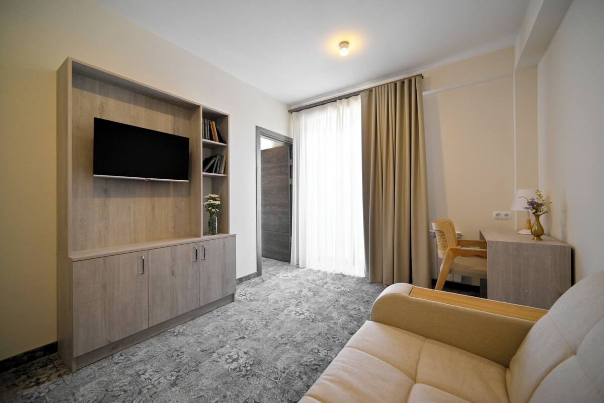 A modern living room with a flat-screen TV, a sofa, a wooden cabinet, and a small table with a vase.