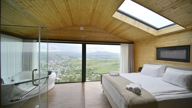 Una camera da letto con un letto grande, una cabina doccia in vetro e vista su una valle.