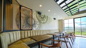 Un ristorante moderno con soffitto alto, ampie finestre e un murale di un fungo sulla parete.