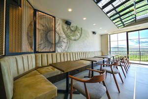A modern restaurant with a high ceiling, large windows, and a mural of a mushroom on the wall.