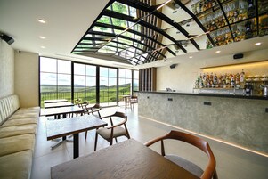 A modern restaurant with a high ceiling, large windows, and a bar area.