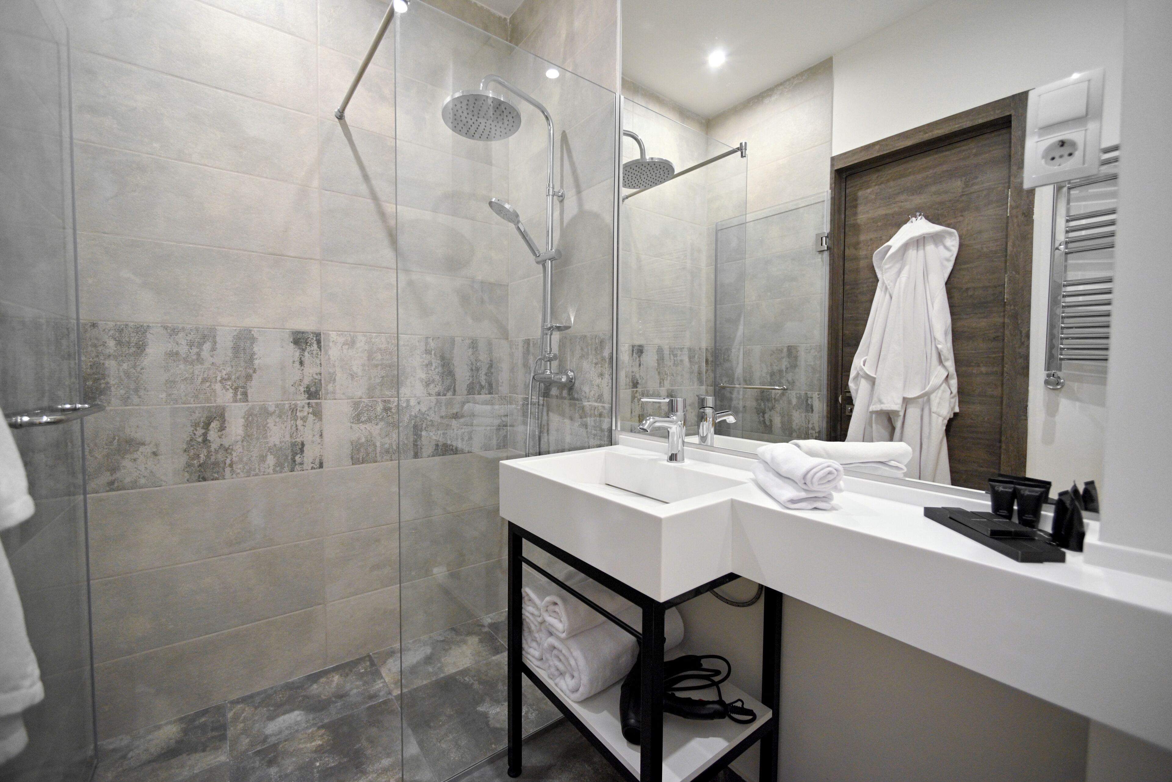 A modern bathroom with a glass-enclosed shower, a white sink with a mirror above, and a towel rack.