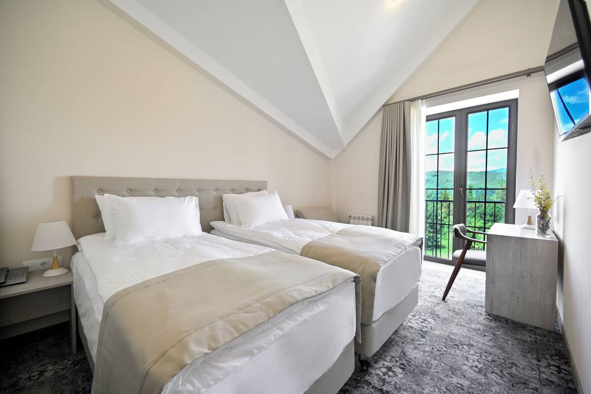 A hotel room with two beds, a desk with a lamp, a chair, and a TV mounted on the wall.