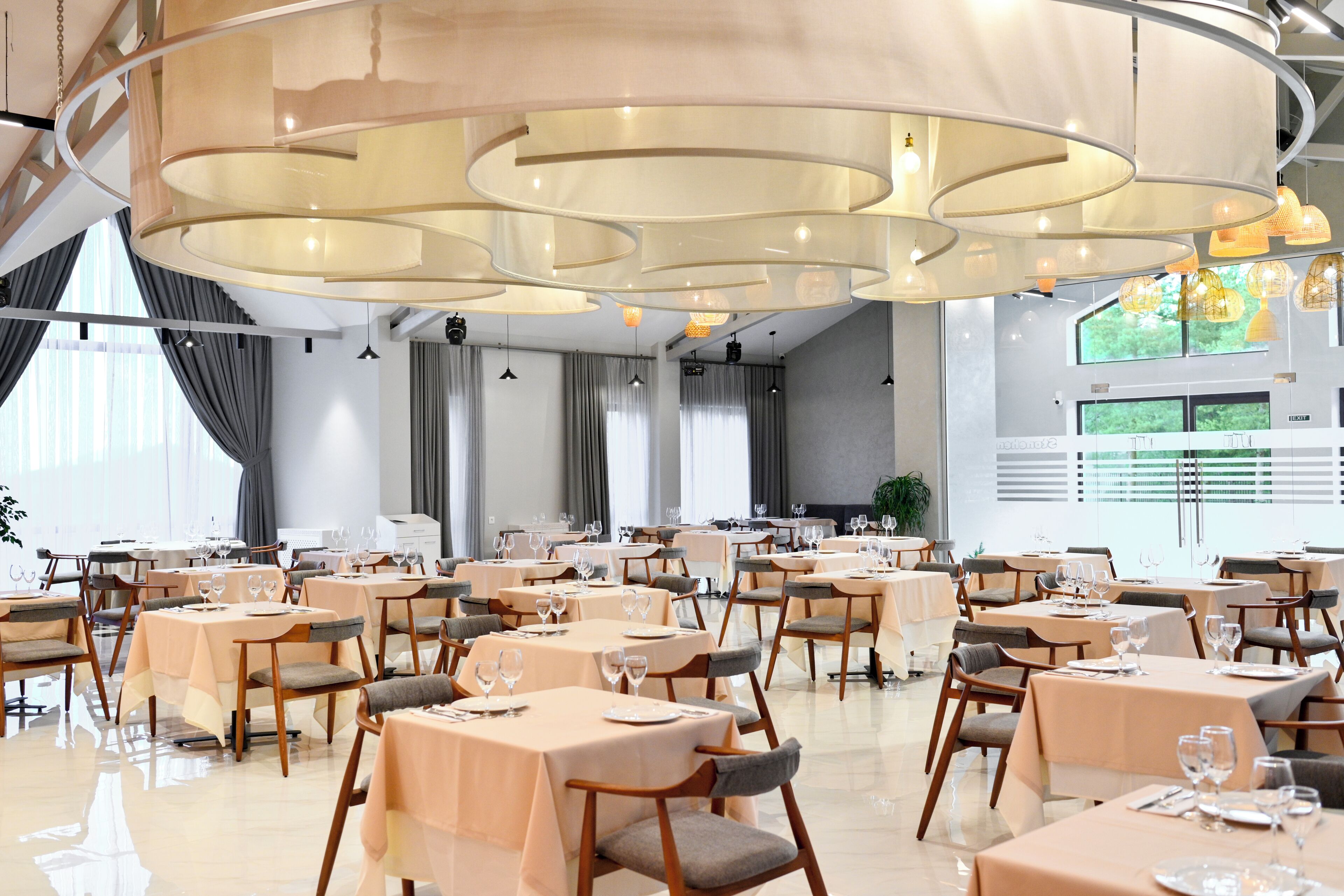 Un vaste espace dédié à la salle à manger, avec de nombreuses tables et chaises, de grandes fenêtres et un design moderne au niveau du plafond.