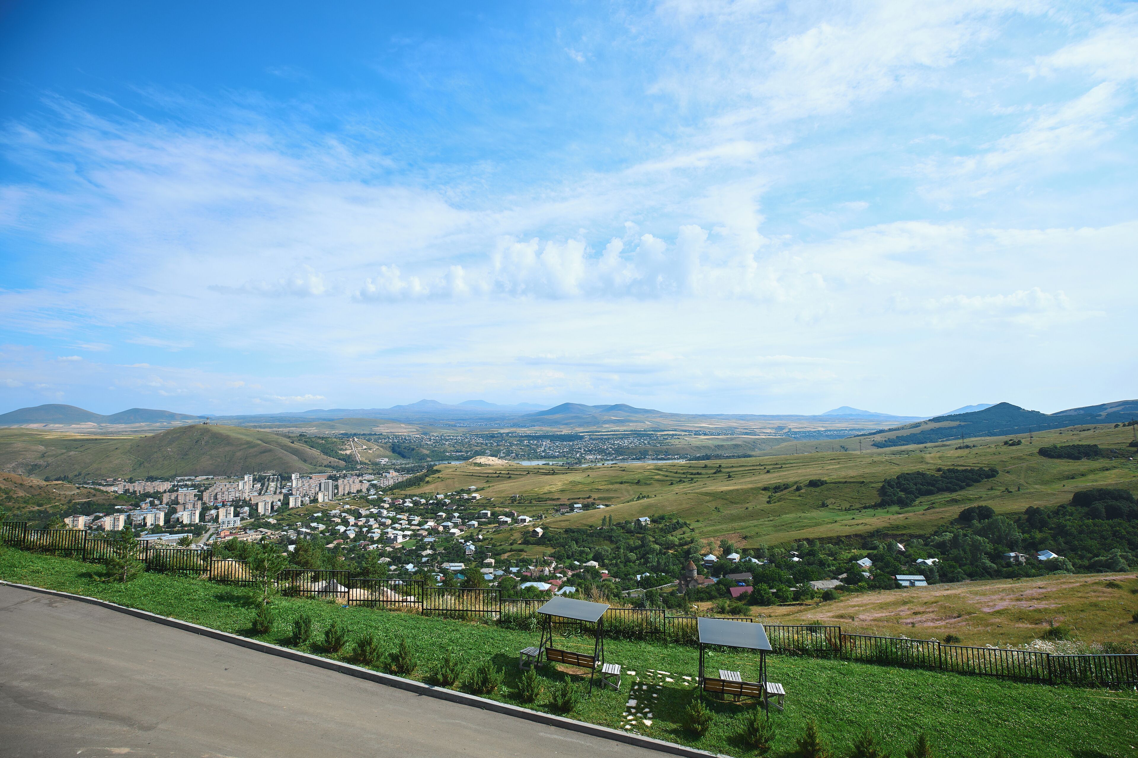 Una vista panorámica de un pueblo con edificios residenciales y comerciales, rodeado de colinas verdes y un cielo despejado.