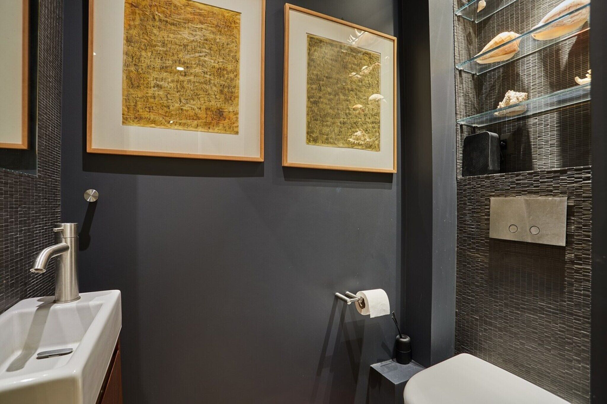 A modern bathroom with a sink, toilet, and framed artwork on the wall.