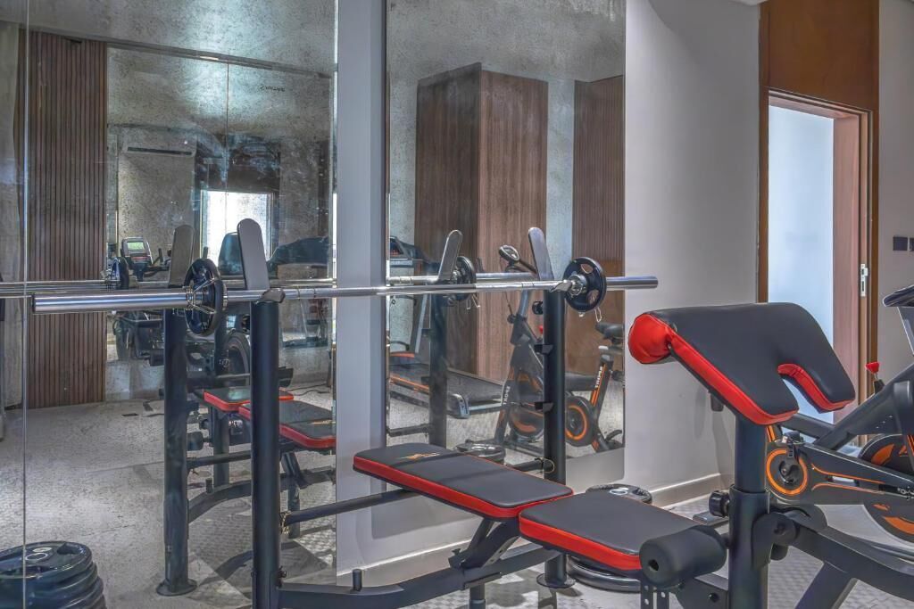 A gym with weightlifting equipment, benches, and a mirror reflecting the interior.