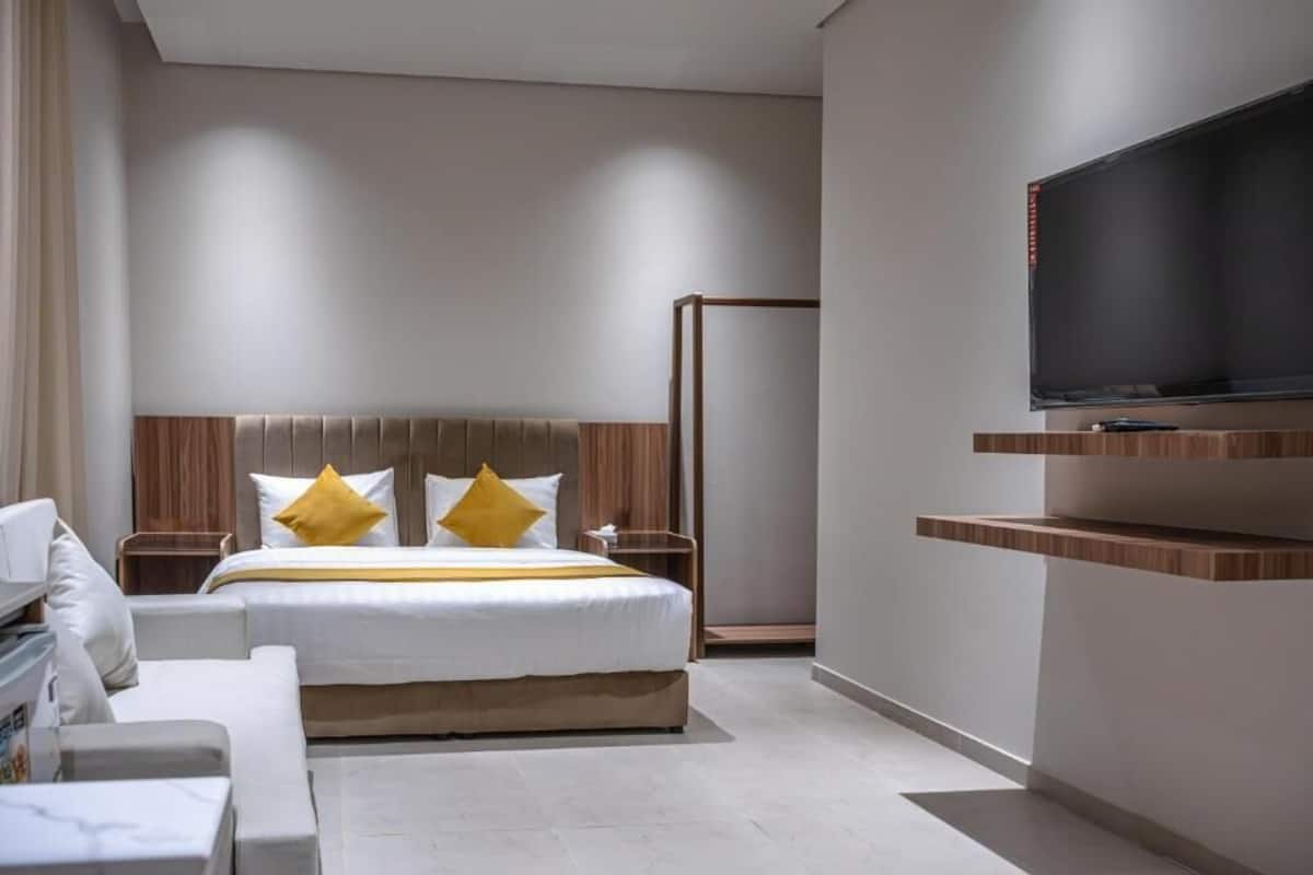 Une chambre d’hôtel moderne avec un grand lit, un téléviseur fixé au mur et une tête de lit en bois.