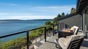 A balcony with a view of a lake, a fire pit, and outdoor furniture. - The Shoreside Serenity Retreat at Indianola Beach (Indianola)