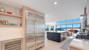 A modern kitchen with a large refrigerator, a dining area with a view, and a bar area. - The Shoreside Serenity Retreat at Indianola Beach (Indianola)
