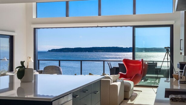 A modern kitchen with a large island, a dining area with a red chair, and a view of the water. - The Shoreside Serenity Retreat at Indianola Beach (Indianola)