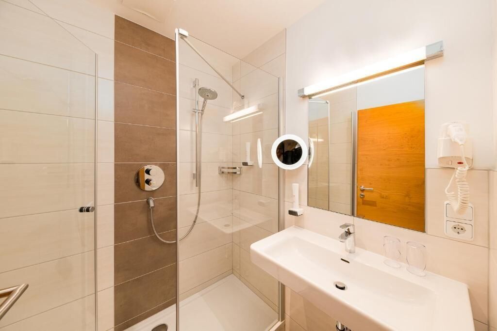 A modern bathroom with a glass-enclosed shower, a white sink, and a mirror with a round frame.