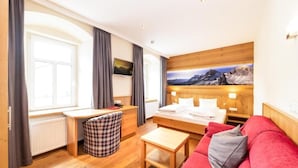 Une chambre d’hôtel avec un lit, un canapé rouge, un bureau, une chaise et un téléviseur.