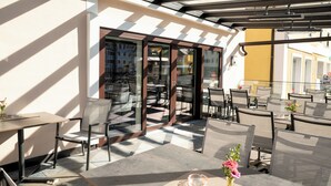 Un espace extérieur aménagé avec des tables et des chaises, une entrée avec une porte vitrée et une vue sur la rue.