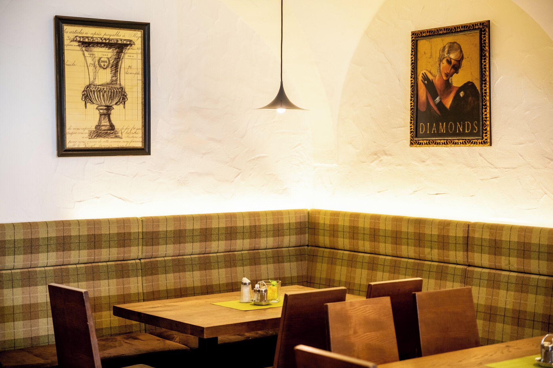 A restaurant interior with a checkered booth seating area, a table with a candle and a glass, and framed artwork on the walls.