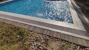 Ein Schwimmbecken mit klarem, blauem Wasser, umgeben von einer Steingrenze und einer Rasenfläche.