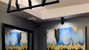 Ein modernes Zimmer mit einer weißen Konsole, zwei abstrakten Gemälden, einer schwarzen Chandelierleuchte und einem grauen Schrank.