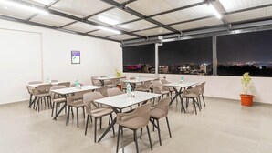 A rooftop dining area with tables and chairs, water bottles, and a potted plant. - Treebo Global Orchid (Mysore)