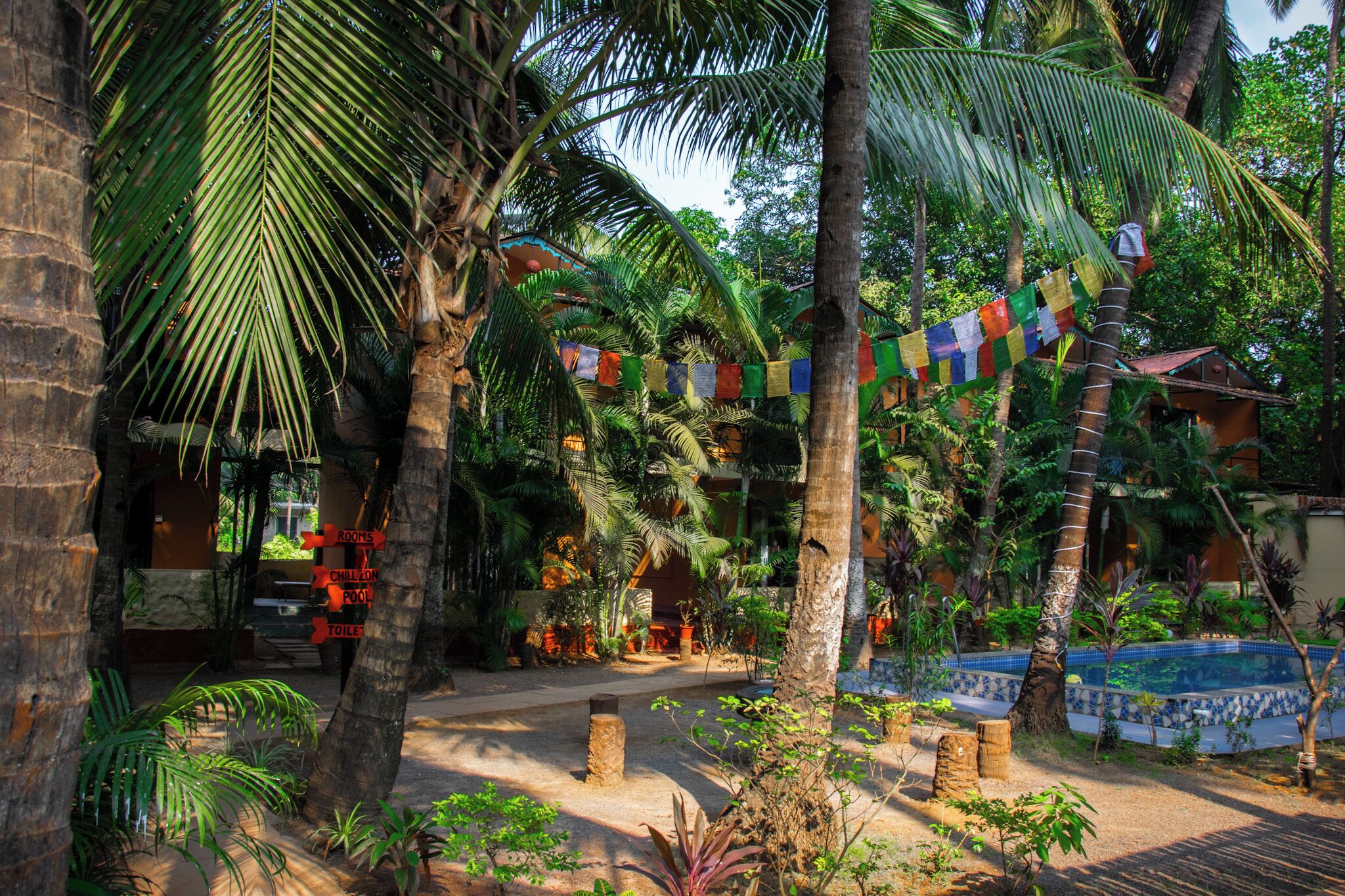 Un resort tropical con palmeras, una piscina y un cartel que indica habitaciones, un espacio para relajarse y un baño.