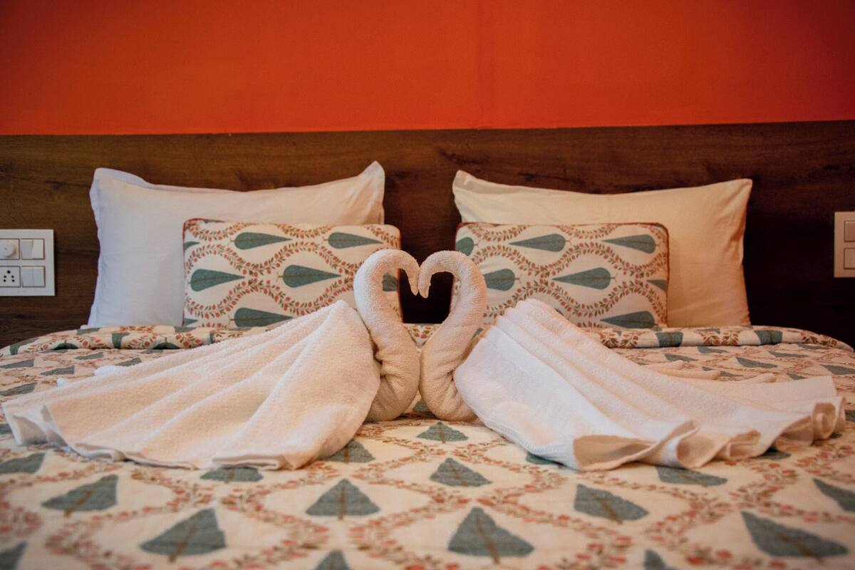 A bed with a heart-shaped towel arrangement, patterned pillows, and a wooden headboard.