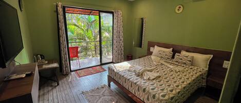 Un dormitorio con cama, escritorio, silla y vista a un espacio exterior por una puerta corredera.