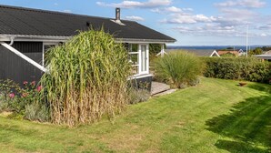 A house with a black roof, white exterior walls, and a chimney. There is a well-maintained lawn with various plants and flowers. - "Tjarven" - 350m from the sea by Interhome (Hejls)