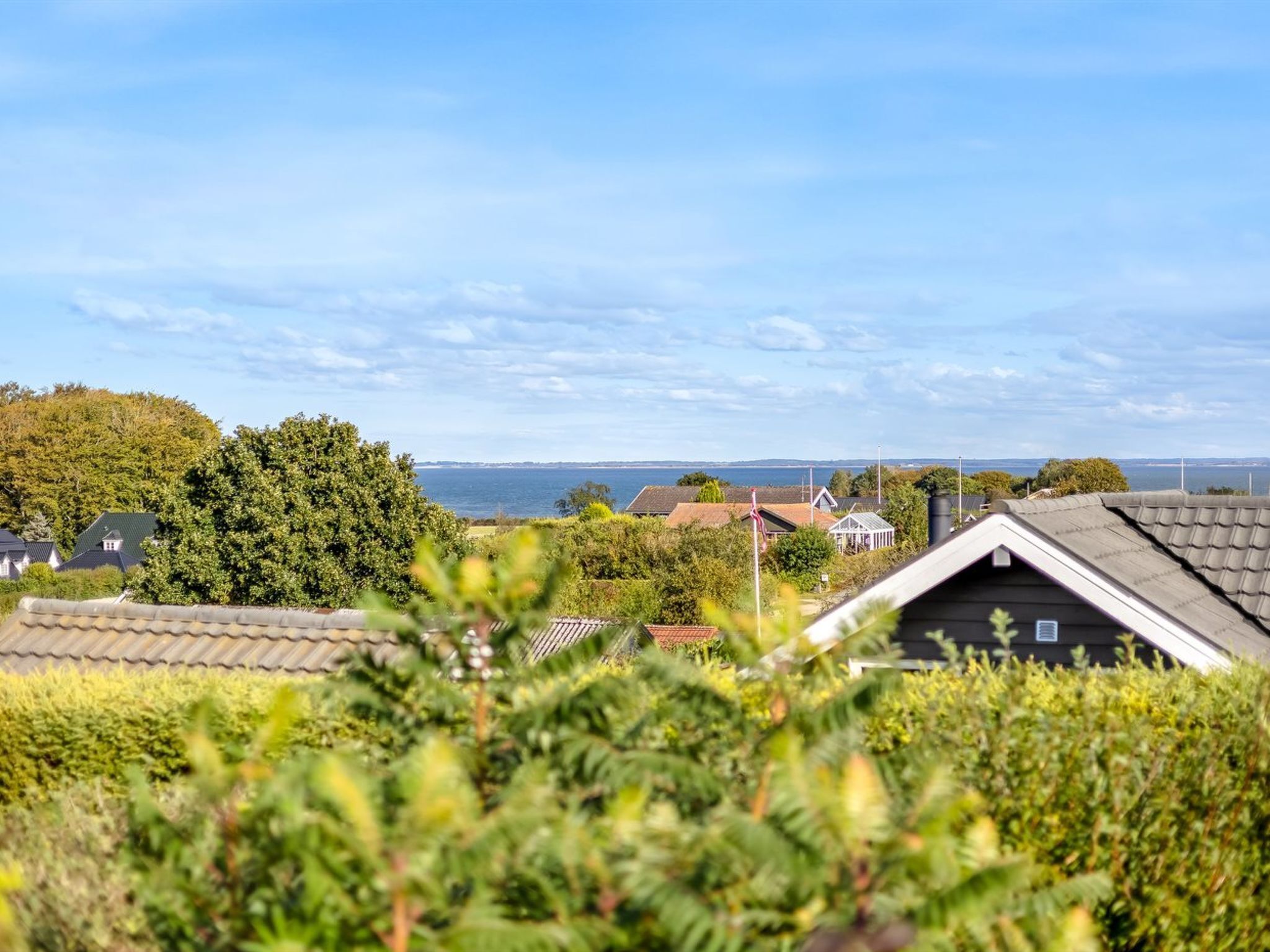 A coastal residential area with houses, a clear sky, and a view of the sea.