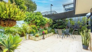 A patio area with potted plants, outdoor seating, and a modern building in the background.